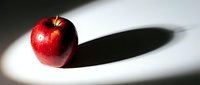 Red apple with dramatic shadow on white surface creating minimalist composition for healthy eating and nutrition concepts.