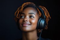 Young African American woman with dreadlocks and radiant smile wearing black headphones against dark background, expressing joy while listening to music.