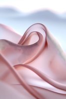 Soft pink silk fabric with gentle folds and waves creating an elegant abstract composition against light blue background, suitable for luxury fashion and beauty designs.