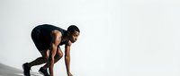 Athletic young African American man in starting position ready to sprint, wearing black sportswear against minimalist white background for fitness motivation.