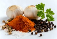 Fresh garlic bulbs with heap of paprika powder, black peppercorns, coriander seeds, sea salt and parsley leaf on white background for cooking and seasoning.
