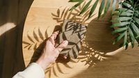 Hand touching tropical palm leaf shadow on wooden surface, creating natural light and shadow play for design and botanical concepts.