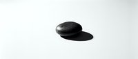 Single smooth black zen stone on white background with soft shadow, minimalist spa and wellness concept in monochrome style.