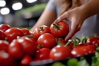Woman selecting fresh red tomatoes at grocery store produce section for healthy cooking and meal preparation.