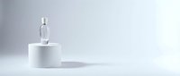 Clear glass bottle with silver cap on white cylindrical podium against minimalist gray background for cosmetic product display and branding mockup.