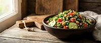 Fresh quinoa tabbouleh salad with cucumber, tomatoes and herbs in rustic bowl on wooden table near window for healthy Mediterranean cuisine recipes.