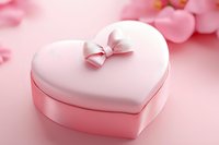 Pink heart-shaped gift box with satin bow on soft pink background, romantic Valentine's day present or jewelry container for special occasions.