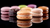 Colorful French macarons in pastel shades arranged in rows with reflection on black surface, focus on peach colored cookie in center, sweet dessert photography.