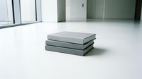 Stack of three gray hardcover books lying on white floor in modern minimalist interior space with large windows and natural lighting for education concepts.