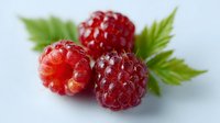 Fresh ripe red raspberries with green leaves on white background, macro shot showing detailed texture and natural dewdrops on berries surface.