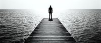 Man standing alone on wooden pier extending into calm water, contemplating horizon in black and white. Suitable for concepts of solitude, reflection, decision-making, and personal journey.