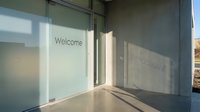 Modern building entrance with frosted glass door featuring Welcome text, concrete walls, and natural sunlight shadows for corporate or hospitality concepts.