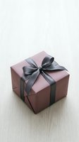 Elegant dusty pink gift box with dark gray satin ribbon bow on white wooden surface, perfect for holiday and celebration concepts.