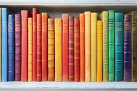 Colorful vintage hardcover books arranged in rainbow order on white wooden shelf, spines showing decorative binding and gold lettering for library or home decor.