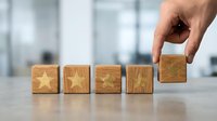 Hand placing wooden cube with golden star completing five-star rating sequence on desk in modern office environment for customer satisfaction surveys.
