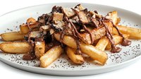 Golden french fries topped with melted chocolate, caramel sauce and crispy wafer pieces on white plate, garnished with cocoa powder for dessert menu.