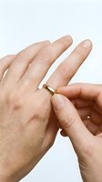 Close-up of a person's hand removing a gold wedding band from their finger against a white background, symbolizing divorce, separation, or relationship change.