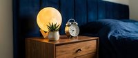 Cozy bedroom nightstand with glowing moon lamp, vintage alarm clock and small plant creating warm ambient lighting for relaxation and sleep.