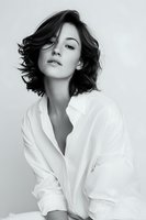 Young woman with tousled bob haircut in white button-up shirt against minimal background, conveying confidence and natural beauty.