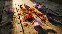 Red saffron spice threads scattered on rustic wooden planks with purple flower petals in warm sunlight for culinary and cooking projects.