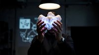 Person with dark skin tone holding glowing digital cube in hands against dark background, representing technology, innovation, and future concepts for business and design projects.