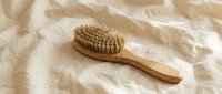 Natural wooden hair brush with boar bristles on soft beige linen fabric for eco-friendly beauty routine and sustainable personal care styling.