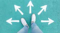 Person in sneakers standing at crossroads with white directional arrows on turquoise ground showing multiple path choices for decision making and life direction.