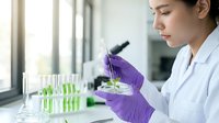 Young female scientist in white lab coat and purple gloves examining plant sample with tweezers in modern laboratory for botanical research and biotechnology studies.