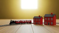 Miniature red toy train with steam locomotive pulling passenger cars approaching small red wooden houses on natural wood surface with warm golden lighting.