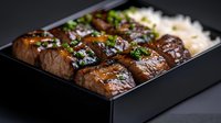 Juicy glazed beef teriyaki slices arranged in black bento box with steamed rice and fresh chopped herbs, close up view showing meat texture and shiny sauce.