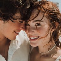 Happy young couple sharing intimate moment with genuine smiles and natural beauty. Romantic connection and joy captured in warm natural lighting.