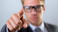 Businessman in suit pointing finger forward against neutral background, conveying leadership and decision-making in corporate environment.
