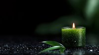 Glowing green aromatherapy candle with bamboo leaf on dark stones background with water drops, creating peaceful spa atmosphere for wellness and meditation.