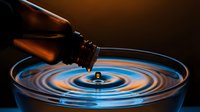 Honey dipper dripping golden honey into glass bowl creating ripples. Natural sweetener flowing from wooden utensil. Organic food ingredient for cooking and baking.