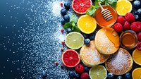 Fresh pancakes with honey, citrus fruits, berries and powdered sugar on dark background. Vibrant breakfast composition with orange, grapefruit and lime slices.