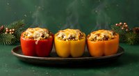 Three colorful stuffed bell peppers with melted cheese on dark plate, festive holiday dinner with pine branches and warm lighting for seasonal cooking.