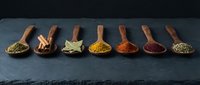 Colorful spices and herbs arranged in wooden spoons on dark slate background for culinary cooking and seasoning recipes.