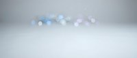 Abstract soft bokeh lights floating above white surface with gentle blue and purple tones creating dreamy atmosphere for backgrounds and overlays.