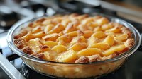 Fresh peach pie with lattice crust baked in glass dish, golden brown pastry and juicy fruit filling creates appetizing homemade dessert on stovetop.
