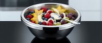 Fresh fruit salad with mixed berries, banana slices and yogurt in modern black bowl on kitchen counter for healthy breakfast or snack preparation.