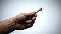 Male hand holding vintage brass key against gradient background symbolizing access, security, solutions and unlocking opportunities in business concepts.