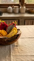 Wooden bowl filled with fresh dragon fruit, mango, and tropical fruits on rustic kitchen table with ceramic containers and windows in background.