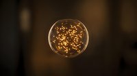 Glowing spherical light bulb with warm golden filament particles floating inside against dark blurred background, suitable for energy and innovation concepts.