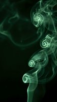 Green smoke swirls with spiral curls rising against a dark black background, creating a mystical and atmospheric abstract effect.