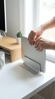 Male hands adjusting laptop screen at bright workspace desk with succulent plant, coffee cup, and wooden organizer near window for ergonomic setup.