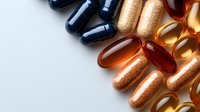 Colorful pharmaceutical capsules and supplements in blue, orange, and gold colors arranged on white background, macro view with copy space for medical designs.