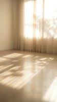Empty room with warm sunlight streaming through window creating soft shadows on wooden floor with beige curtains for interior design and real estate.