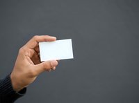 Close-up of hand holding blank white business card against gray background, suitable for corporate branding, contact information display, and professional marketing materials.
