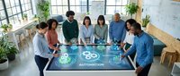 Diverse business team collaborating around futuristic holographic automation interface in modern office workspace with natural lighting.