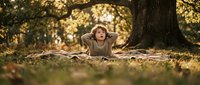 Young woman relaxing on blanket under autumn tree with golden sunlight filtering through leaves, peaceful outdoor lifestyle moment.